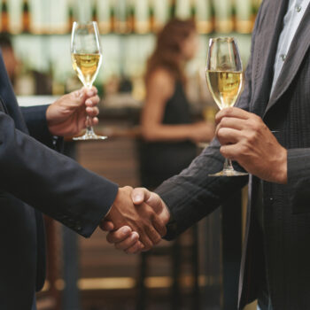 Hands of men shaking hands and drinking white wine