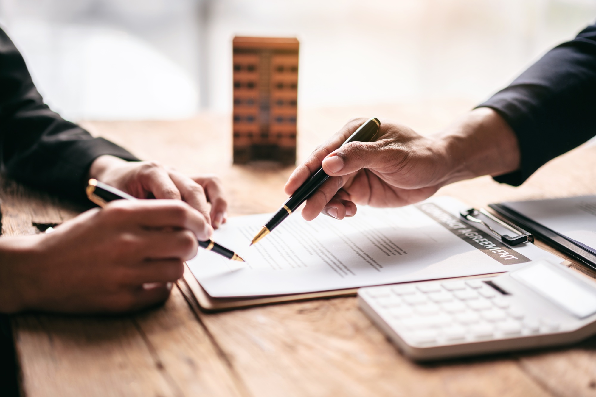 Two people are signing a document on a table