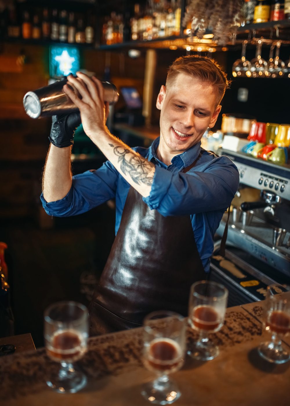 Male bartender in apron works with shaker at the bar counter. Alcohol beverage preparation. Barman occupation