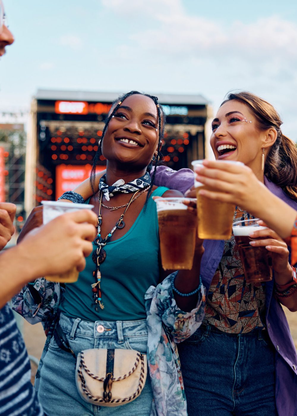 Multiracial group of cheerful friends drinking beer and having fun on open air music concert during summer.